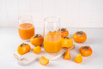 Fresh homemade persimmon juice in portioned glasses, with whole and cut persimmon c in the background