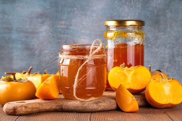 Persimmon jam. Sweet autumn homemade jam or marmalade canning preserves in a jar, with whole and cut persimmon c in the background