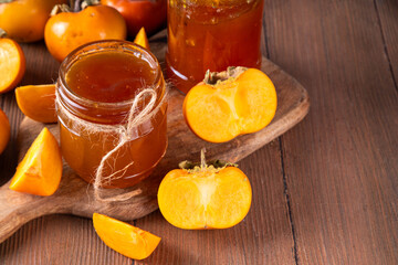 Persimmon jam. Sweet autumn homemade jam or marmalade canning preserves in a jar, with whole and cut persimmon c in the background
