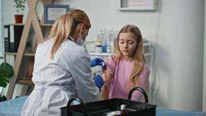 Healthcare worker giving vaccine to child. Serious girl visiting pediatrician