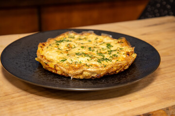 A plate of Cheesy Macaroni and Vegetable Frittata Bake on a black plate placed on a wooden kitchen table