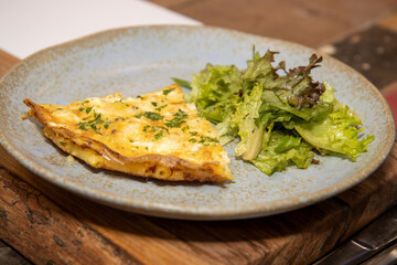A slice of Cheesy Macaroni and Vegetable Frittata Bake on a grey plate placed on a wooden kitchen table