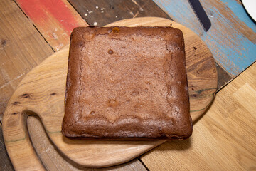 A top down photo of a slab of chocolate brownies that has just been taken out of the oven cooling ready to be cut in to portions and squares on a wooden chopping board on a kitchen table