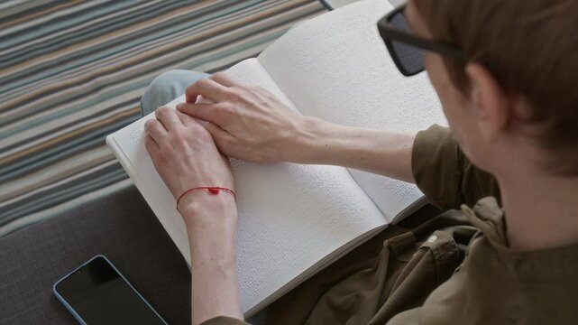High angle view of man with disability reading book with braille dot system while sitting on sofa