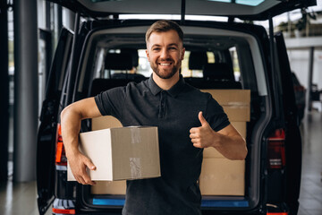 Holding the packed product in hands. Delivery man or loader is near the car with a box