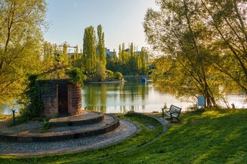 Obraz premium Autumn recreational area by a lake in the city. Warm autumn colors on the leaves of the trees on a sunny autumn day.