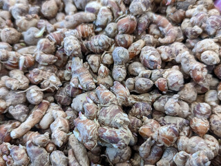 A close-up of a cluster of fresh turmeric roots showcases their vibrant orange interiors, peeking through the rough, earthy brown skin.