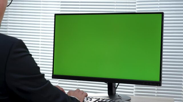 Back view of man using computer with green screen at office. Close-up of business man working on computer monitor with chroma key