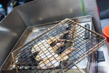 Close-up of dried squid being grilled on a charcoal stove, showcasing traditional Thai street food preparation.