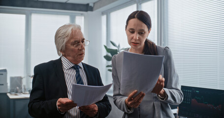 Financial analyst reports to boss about successful deal. Female employee and team leader have discussion, analyze papers, financial documents. Work in modern office of bank or stock exchange company.