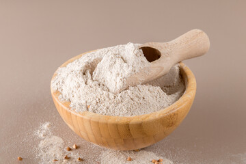 Buckwheat flour in a wooden bowl and raw buckwheat grain on beige monochrome background. Alternative flour, gluten free flour, healthy nutrition