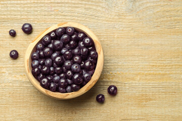 Ripe acai berries in bowl on wooden table, top view. Space for text