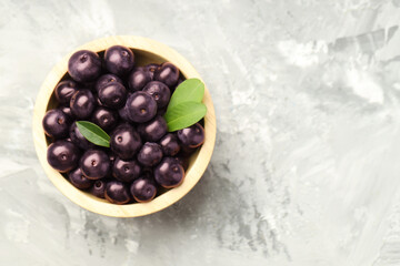 Ripe acai berries and leaves in bowl on grey textured table, top view. Space for text