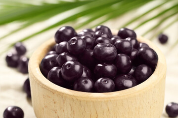 Ripe acai berries in bowl on table, closeup