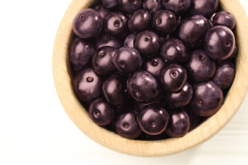 Ripe acai berries in bowl on white wooden table, top view