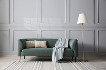 Comfortable sofa and lamp near grey wall in room