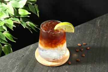 Refreshing espresso tonic drink with slice of lime and coffee beans on dark table