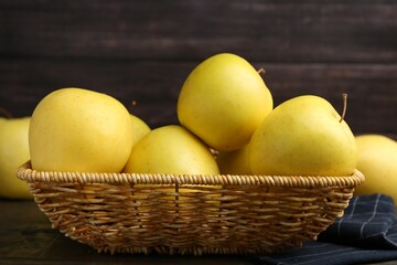 Fresh yellow apples in wicker basket on table, closeup