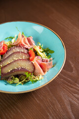 A gourmet salad featuring tomatoes and wine-marinated pear, elegantly presented on a blue plate. Ideal for themes of fine dining, healthy eating, and culinary artistry
