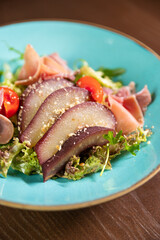 A gourmet salad featuring tomatoes and wine-marinated pear, elegantly presented on a blue plate. Ideal for themes of fine dining, healthy eating, and culinary artistry