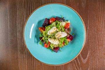 A delicious salad with mozzarella, beetroot, tomato, and fresh salad leaves, beautifully presented on a blue restaurant plate. Perfect for themes of healthy eating, gourmet dining, and fresh, vibrant 