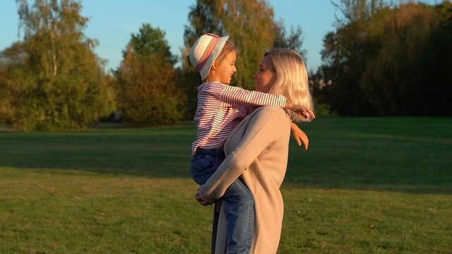 Happy family walk outdoors mother holds on hands daughter in autumn park at sunset. Weekend leisure.