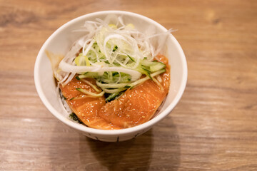 Delicious bowl of sesame salmon topped with fresh greens and herbs, served in a stylish white container on a wooden table.