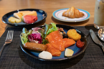 Delicious breakfast spread featuring fresh salad, salmon, fruits, and a croissant on a wooden table.