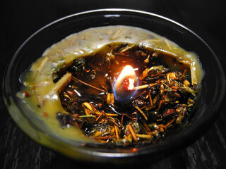 Burning herbal ritual candle made of natural beeswax and plants on black wooden surface for white...