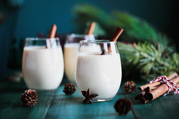 Three glasses of creamy eggnog with cinnamon sticks and star of anise. Selective focus with blurred festive background.