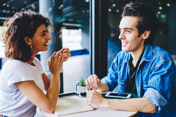 Friendly warm meeting of hipster guys dressed in casual wear in cafeteria.Positive young man with cheerful female blogger discudding funny publication and plan of cooperation in cafe
