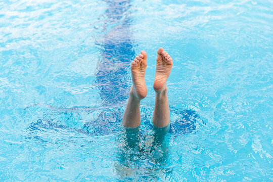 child practicing handstands in a public pool with wrinkled feet sticking out of the water