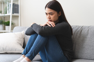 Fototapeta premium Unhappy anxiety young Asian woman covering her face with pillow on the cough in the living room at home.