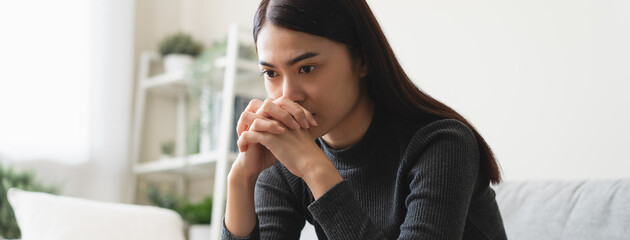Fototapeta premium Unhappy anxiety young Asian woman covering her face with pillow on the cough in the living room at home.
