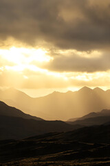 Obraz premium Golden light casts a warm glow over distant mountains, creating a serene landscape with soft contours and dramatic lighting effects