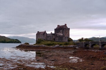 The famous medieval scottish Eilean Donan castle standing on the sea shore during low tide with grey moody autumn rainy atmosphere evokes harsh medieval times of Scotland. Isle of Skye