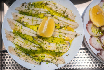 Pickled anchovies with garlic and parsley marinated in vinegar in a round wooden plate on a white...