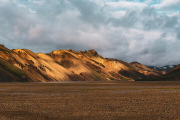 Breathtaking moment in Rainbow mountains near the Landmannalaugar area of Iceland with dramatic lights at the end of the day with clouds and scenic nordic nature enlightened with last sun rays.