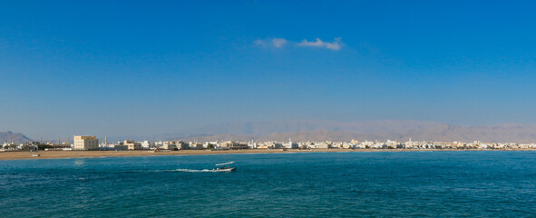 A serene view of Sur Oman with traditional boats gliding across the blue waters on a clear sunny day