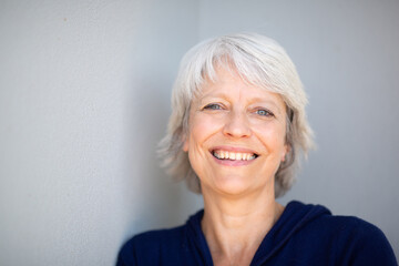 Happy mature woman leaning against gray wall