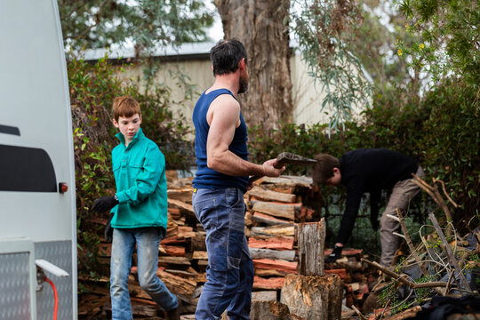 Man splitting wood for fire with son helping him stack firewood for winter