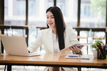 Fototapeta premium Beautiful Asian businesswoman focused on reviewing documents in a modern office.