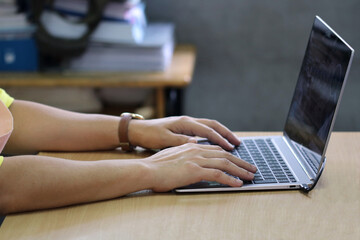 A woman is typing on a laptop, showing her dedication to her work in an environment full of textbooks.