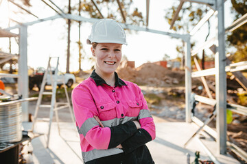 A young woman with arms crossed standing and smiling at the camera on worksite