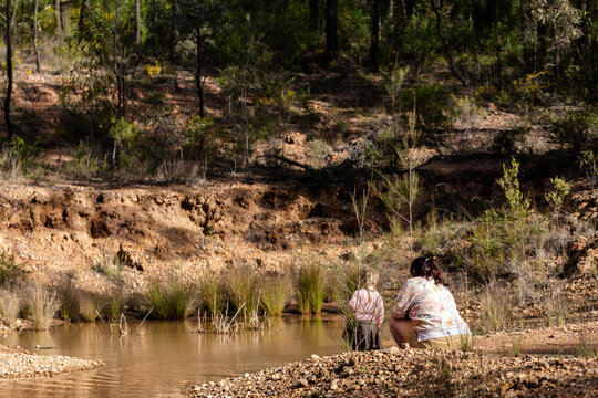 Teen girl with her young niece exploring australian bush squatting down by waterhole in bushland