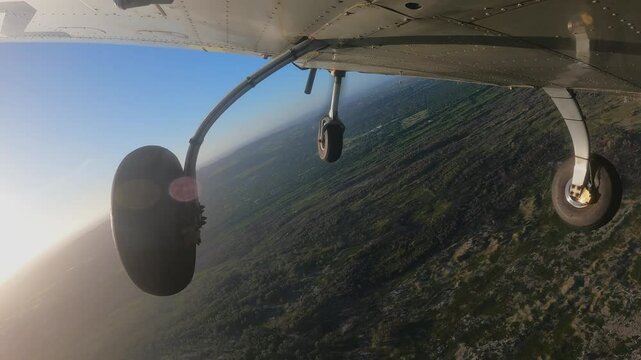 Light three wheels training airplane doing right turn flying over the bushes. Closeup view on the main landing and front gears. View from the bottom of aircraft.