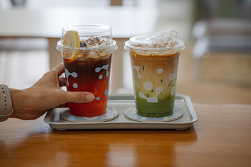 hand of woman holding a take-out iced tea honey lemon on table at coffee shop
