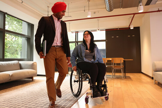 Businessman wearing Sikh turban and businesswoman on wheelchair in office