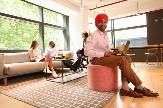 Businessman wearing Sikh turban sitting with laptop in office