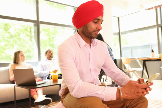Businessman wearing Sikh turban sitting with phone in office